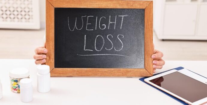 nutritionist-holding-small-blackboard-with-words-weight-loss-table-clinic-closeup_495423-115246